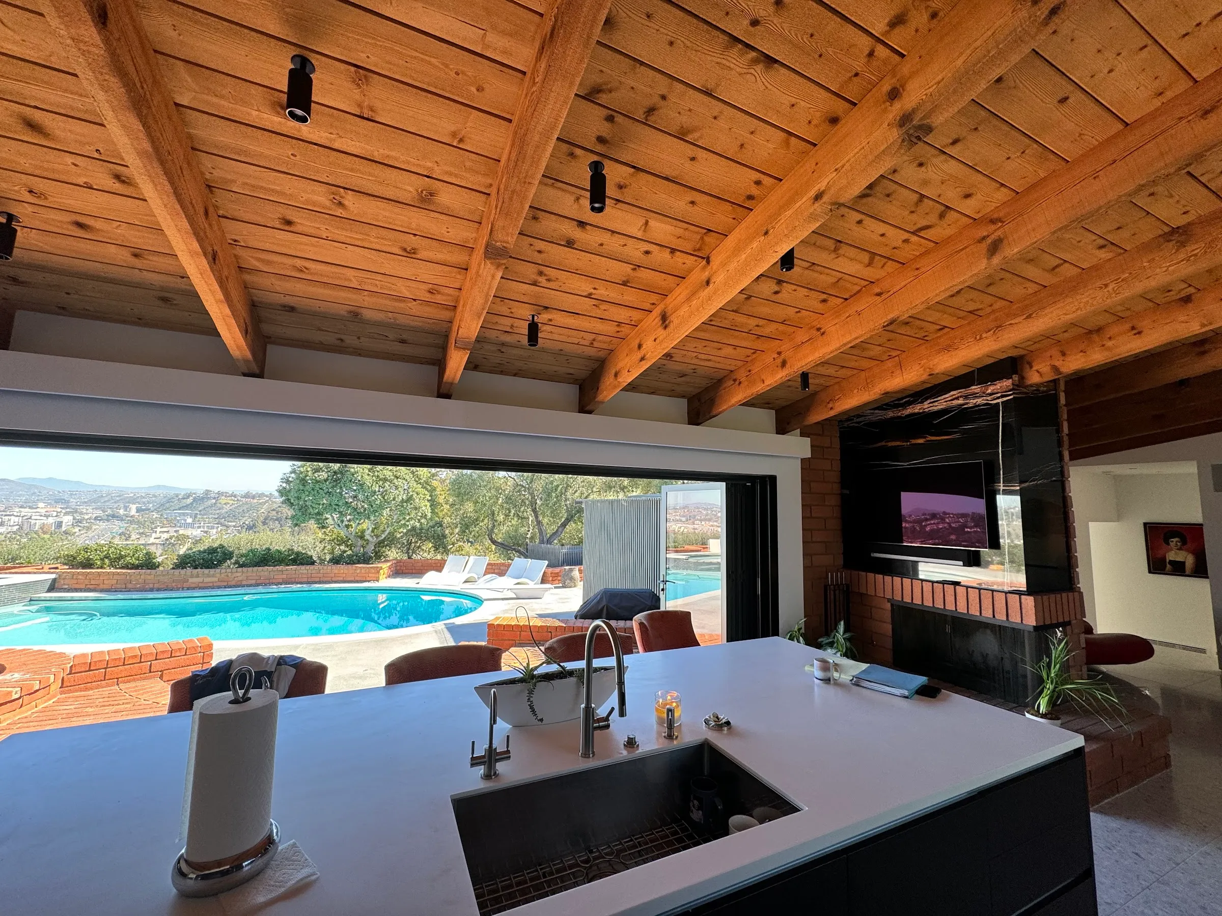 An indoor-outdoor kitchen with beam lighting, open to the pool