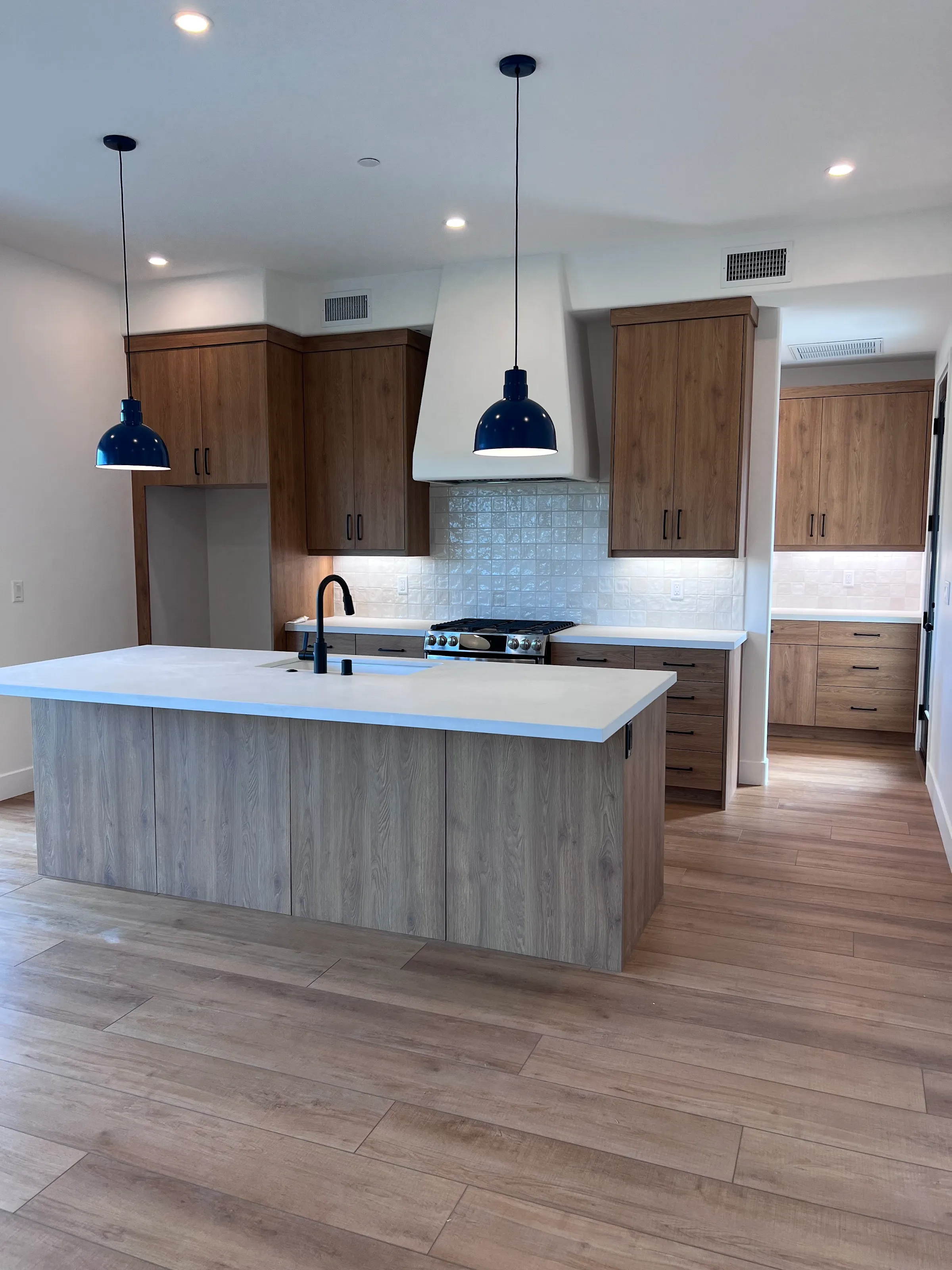 A kitchen island under a pair of pendant lights with recessed lighting