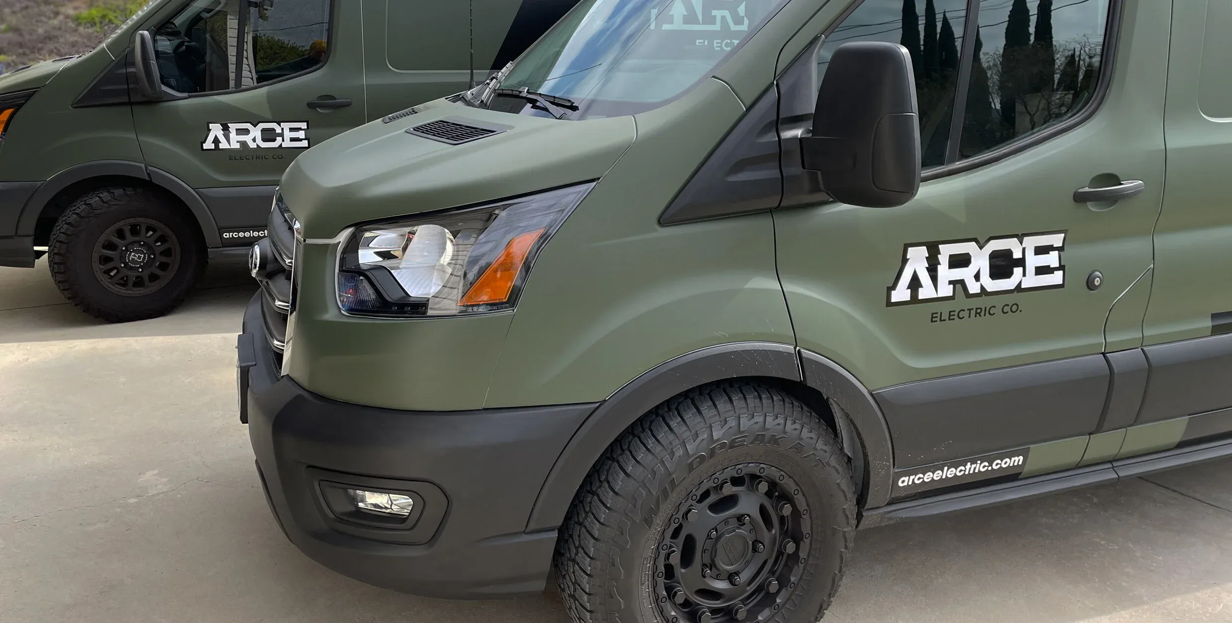 Two olive Arce Electric vans with the ARCE logo